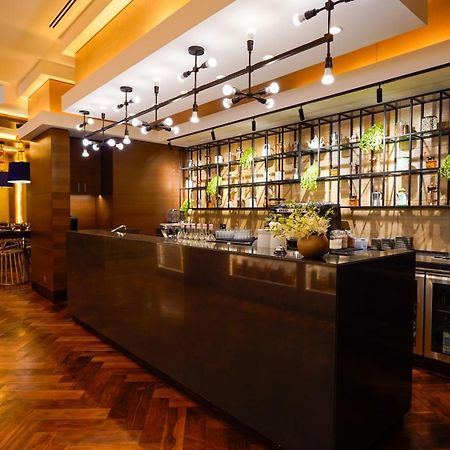 Jabal Omar Hyatt Regency Makkah Hotel Mekka Eksteriør billede The photo shows a modern bar area in a restaurant. The bar features a sleek, dark countertop and is backed by a decorative arrangement of shelves that holds various bottles and plants. The lighting is warm and stylish, with multiple hanging pendant l