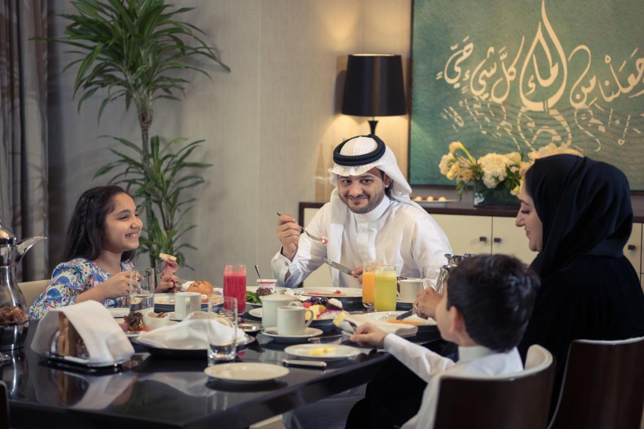 Jabal Omar Hyatt Regency Makkah Hotel Mekka Eksteriør billede The photo depicts a cheerful family gathered around a dining table for a meal. They appear to be enjoying breakfast or a brunch. The table is set with various dishes and drinks, including juices and plates of food. 

A man wearing traditional attire 