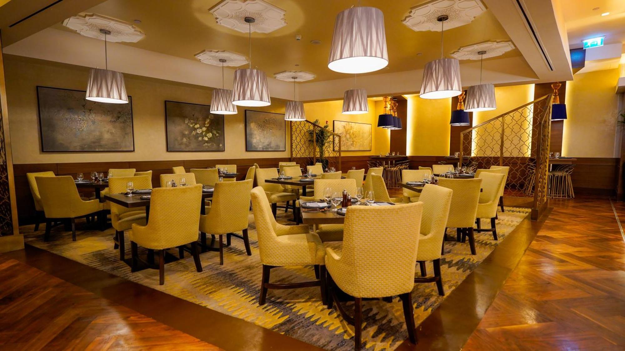 Jabal Omar Hyatt Regency Makkah Hotel Mekka Eksteriør billede The photo shows an elegant restaurant interior. There are several tables arranged with yellow upholstered chairs, creating a warm and inviting atmosphere. Soft lighting is provided by modern pendant lamps hanging from the ceiling. The floor features 