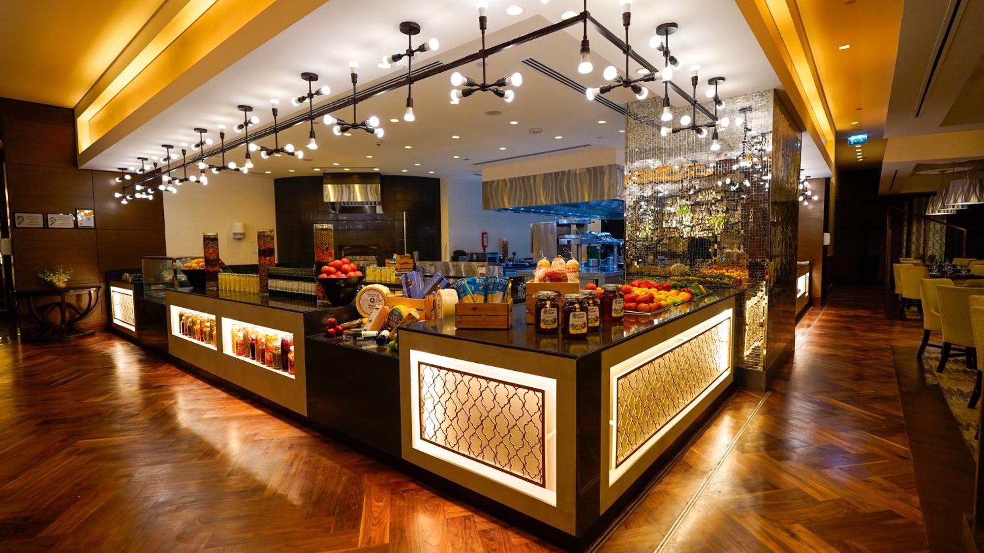 Jabal Omar Hyatt Regency Makkah Hotel Mekka Eksteriør billede The photo shows a stylish and modern buffet area in a restaurant or hotel. The design features a sleek counter with various food items displayed, including fresh fruits. The space is well-lit with pendant lights hanging from the ceiling, creating a w