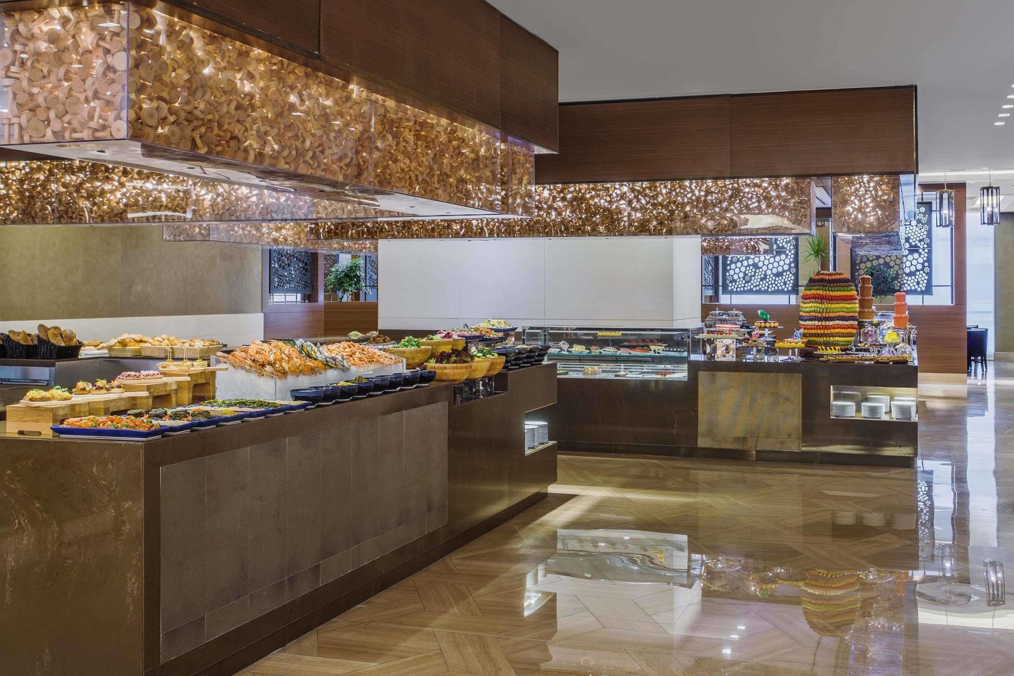 Jabal Omar Hyatt Regency Makkah Hotel Mekka Eksteriør billede The photo shows an elegant buffet setup in a spacious dining area. There are various food displays arranged on sleek surfaces, including an assortment of items such as pastries, fruits, and possibly other dishes. The decor features warm lighting with
