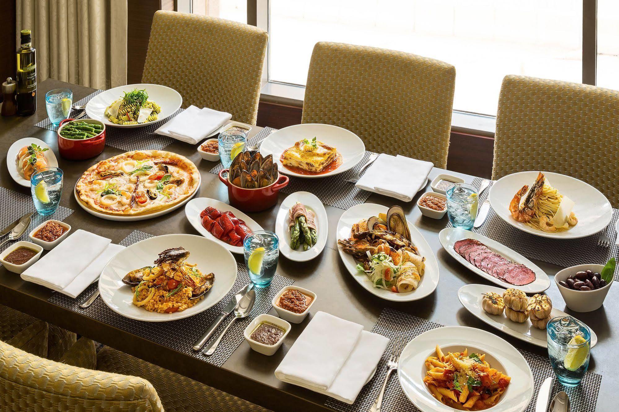 Jabal Omar Hyatt Regency Makkah Hotel Mekka Eksteriør billede The photo shows a large dining table set with various dishes, suggesting a festive or communal meal. There are several plates of food including:

- A pizza topped with vegetables and possibly meats.
- A serving of lasagna.
- A variety of pasta dishes