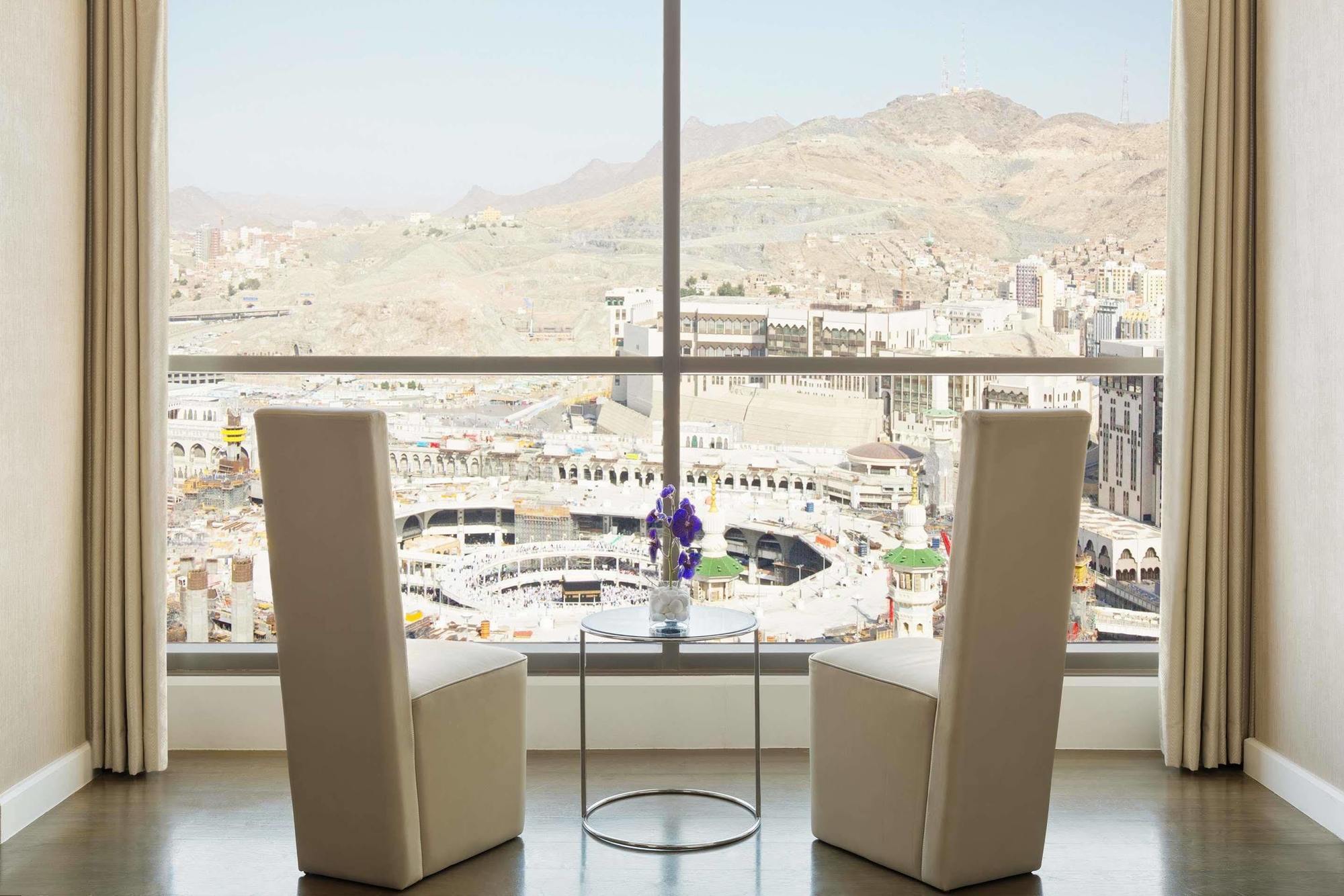 Jabal Omar Hyatt Regency Makkah Hotel Mekka Eksteriør billede The photo shows a modern indoor setting with two tall, white chairs positioned facing a large window. Through the window, there is a panoramic view of a cityscape that includes mountainous terrain and buildings, suggesting it may be a notable locatio
