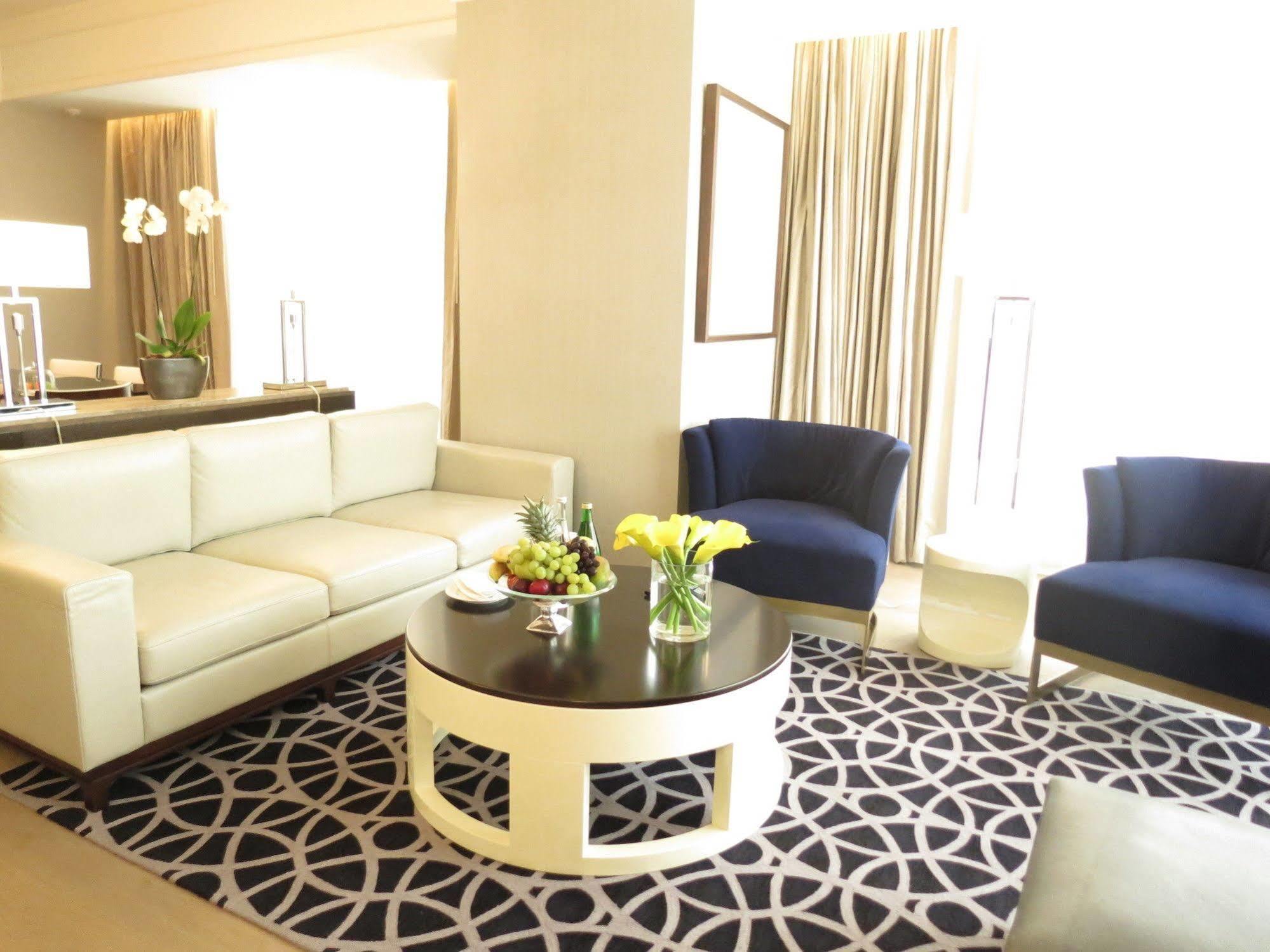 Jabal Omar Hyatt Regency Makkah Hotel Mekka Eksteriør billede The photo shows a stylish and modern living area. It features a white sectional sofa, two blue upholstered chairs, and a round black coffee table with a decorative centerpiece that includes flowers and fruits. The flooring is covered with a patterned