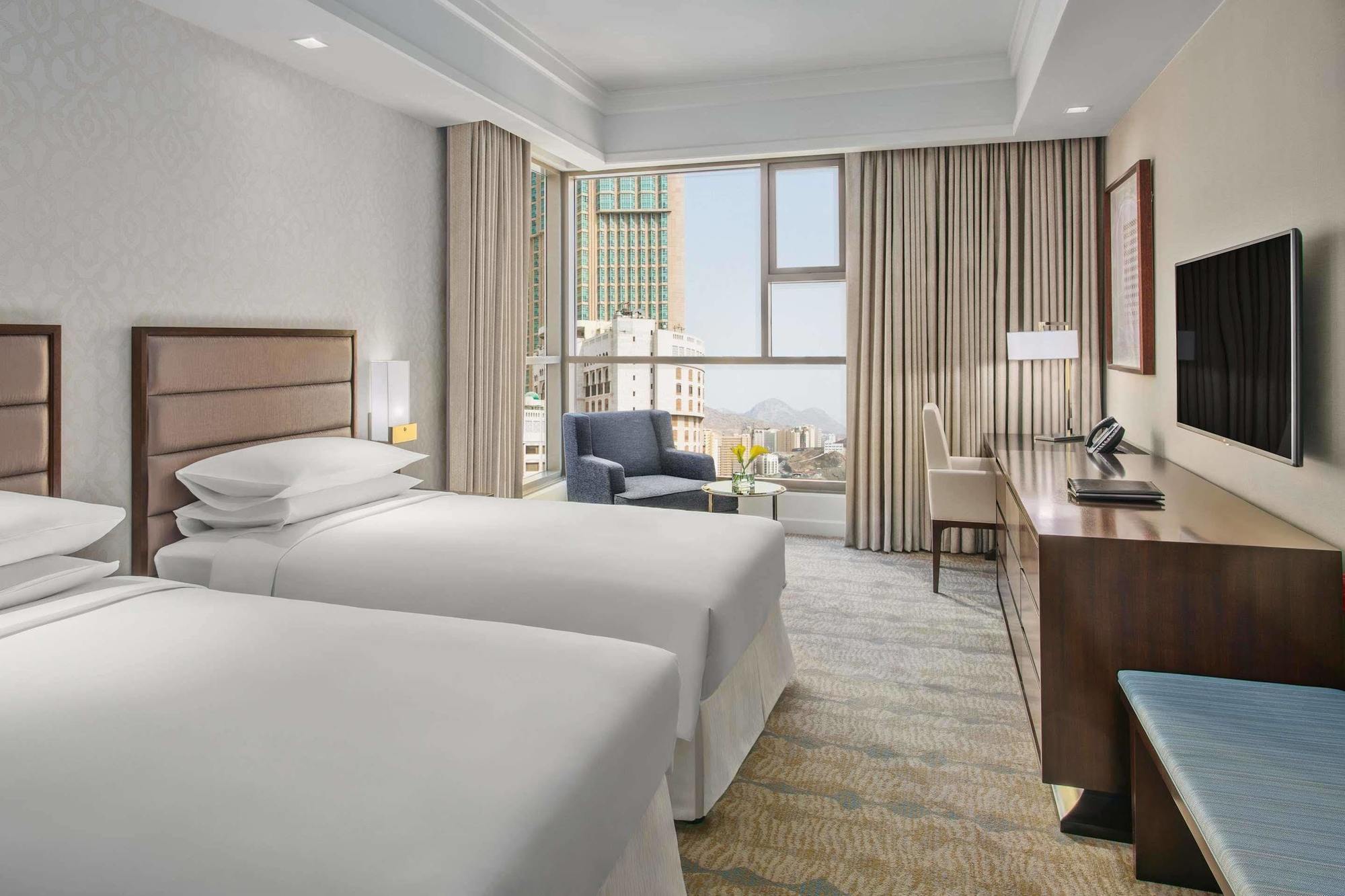 Jabal Omar Hyatt Regency Makkah Hotel Mekka Eksteriør billede The photo shows a modern hotel room featuring two single beds with white bedding. There's a spacious window allowing natural light to fill the room, which is adorned with light-colored curtains. In one corner, there's a comfortable armchair next to a