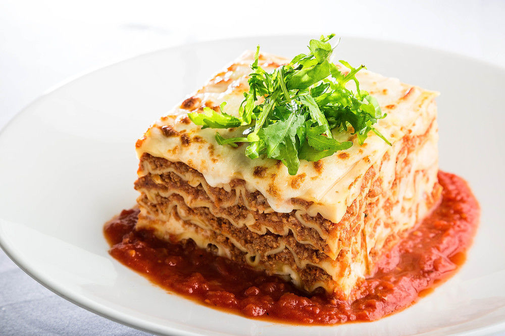 Jabal Omar Hyatt Regency Makkah Hotel Mekka Eksteriør billede The photo shows a serving of lasagna, which is a layered pasta dish. The lasagna has multiple layers, with a combination of meat, cheese, and béchamel sauce, topped with a sprinkle of fresh green herbs. It sits on a plate with a rich red tomato sauce