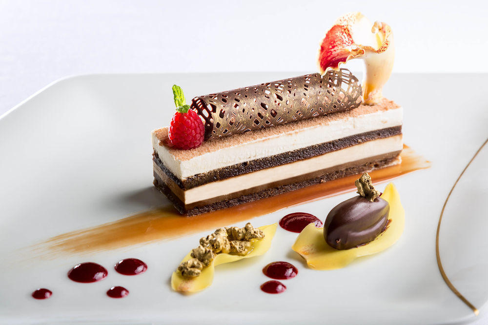 Jabal Omar Hyatt Regency Makkah Hotel Mekka Eksteriør billede The photo showcases an elegantly plated dessert. It features a layered cake with different textures and flavors, including chocolate and cream layers. The dessert is topped with a decorative chocolate tube and garnished with fresh raspberries and a s