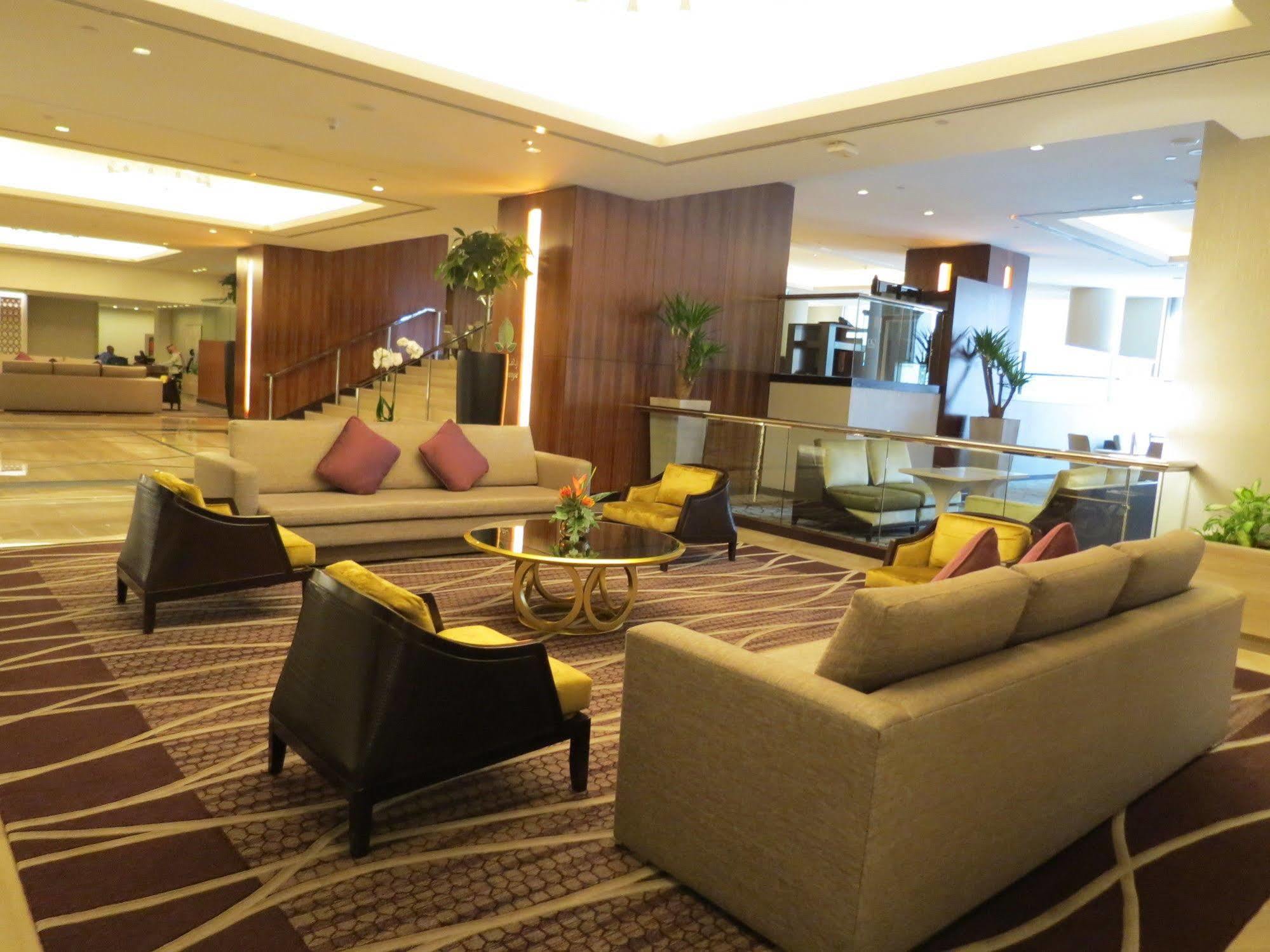 Jabal Omar Hyatt Regency Makkah Hotel Mekka Eksteriør billede The photo shows a modern and stylish lobby or lounge area. It features two large sofas with a light color and several cushions in shades of purple. There are also two armchairs with a darker finish and yellow cushions. In the center, there is a round